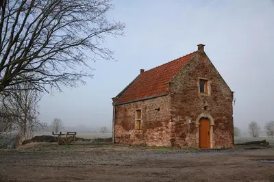 an old brick building with a red roof at Bakkershuisje Kraneveldhoeve in Haacht