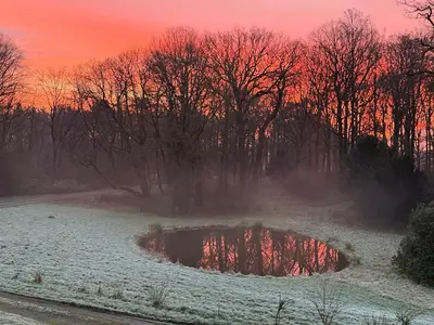 a snow covered field with a pond in front of a sunset at Logies Het Koetshuis in Herentals
