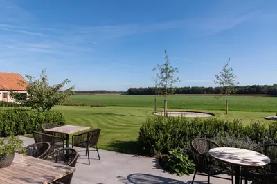 a patio with tables and chairs and a green field at Logies De Hoeven in Kasterlee