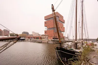 a boat is docked in a river with a tall building at SHWAY - The Second Mate's Glance in Antwerp