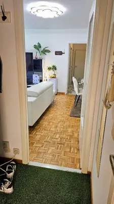 a living room with a white couch and a wooden floor at Chambre meublée chez l'habitant a uccle in Brussels