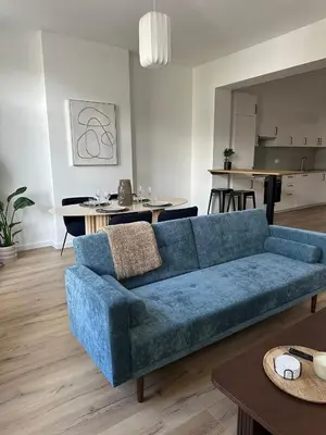 a living room with a blue couch and a kitchen at 1- Nid lumineux 2 chambres au coeur d'Ixelles in Brussels