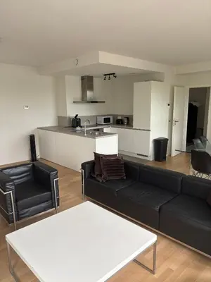 a living room with a black couch and a kitchen at Modern City Apartment Close to Everything in Brussels