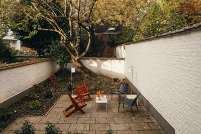 a patio with chairs and a tree next to a wall at La Villa Maurice in Brussels