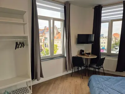 a bedroom with a bed and a table and windows at Studios - European Quarter in Brussels