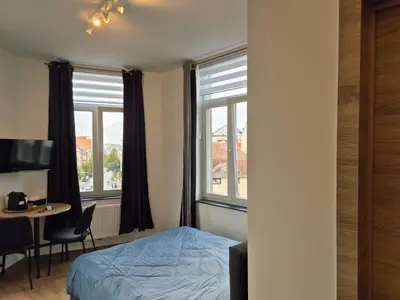 a bedroom with a bed and a table and two windows at Studios - European Quarter in Brussels