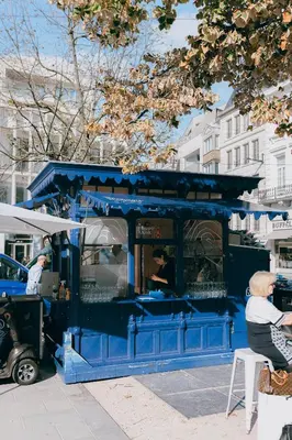 a blue food cart with a man sitting on a chair at Kouter House in Ghent