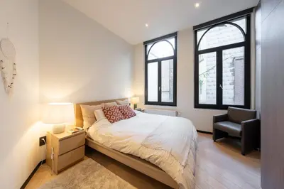 a bedroom with a bed and a chair and windows at A Marbled Touched Haven in Antwerp