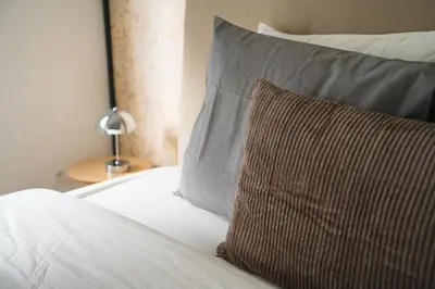 a bed with white sheets and a brown pillow at Lovely 1BR & 1LR Apt for 4P, Only 15 Min Walk to City Center in Ghent