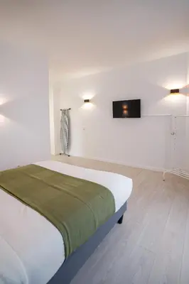 a white bedroom with a bed and a tv on the wall at Jourdan 4 in Brussels
