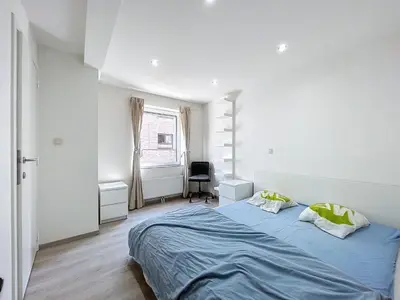 a white bedroom with a blue bed and a window at kazernestraat app 101 in Ghent