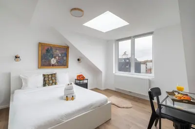a white bedroom with a bed and a desk and a window at Brussels Louise Design residence in Brussels