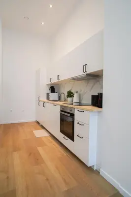 a kitchen with white cabinets and a wooden floor at Appartment St guidon 1 in Brussels