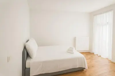 a white bedroom with a bed with white sheets at Cozy Brabanconne apartment in Brussels