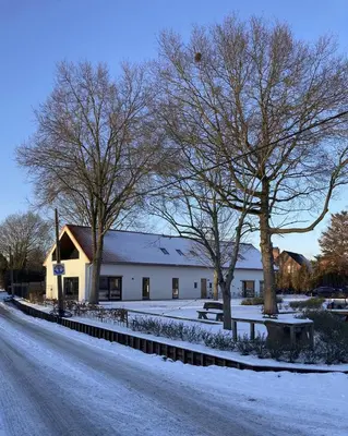 a building with snow on the ground next to a street at De Kempische Hoef in Westerlo