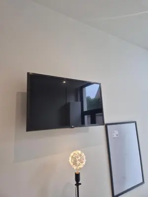 a flat screen tv on a wall with a lamp at Huis ALNA 10 in Mechelen