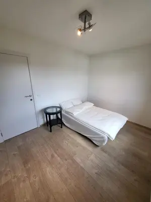 a white bedroom with a bed and a table at Ruim appartement met terras in Ghent