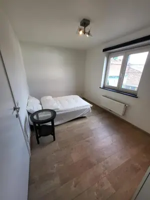 a bedroom with a bed and a table and a window at Ruim appartement met terras in Ghent