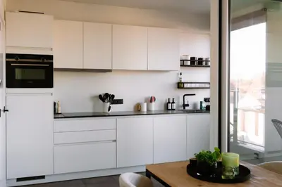 a kitchen with white cabinets and a wooden table at La Petite Foret Stylish City Apartment Ghent in Ghent
