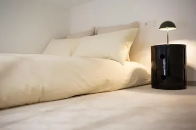 a bed with white sheets and a black lamp at Charmant studio avec mezzanine et terasse in Brussels