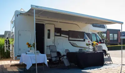 a white camper with a table and a tent at Camper max 5p, unique experience, terras, central Belgium in Denderleeuw