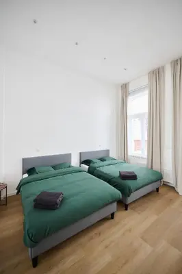 two beds in a white room with green sheets at Toison d'Or & saunna 2 in Brussels