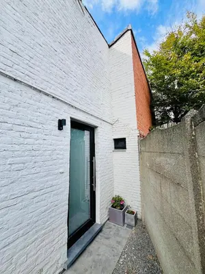 a white brick building with a door and a fence at Ruime studio met eigen ingang en private badkamer in Opwijk