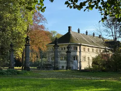 an old house with a fence in the grass at Logies Het Koetshuis in Herentals