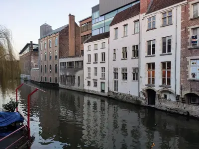 a canal with buildings and a boat in the water at Unique Historic Mill Loft with River Lys Views in Ghent