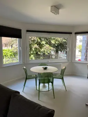 a living room with a table and chairs and two windows at Knus appartement centrum Gent in Ghent