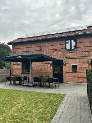 a building with tables and umbrellas in front of it at Zeer ruime groepswoning voor 24p in Turnhout