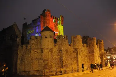 a large castle at night with people walking around it at De Draecke Hostel in Ghent