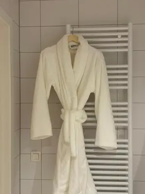 a white robe hanging on a rack in a bathroom at L'Excelsior Suites in Brasschaat