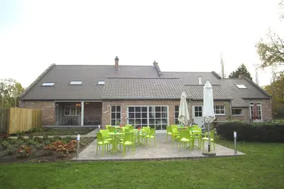 a house with a patio with green chairs and an umbrella at Bed & Breakfast De Kleine Magnolia in Tessenderlo