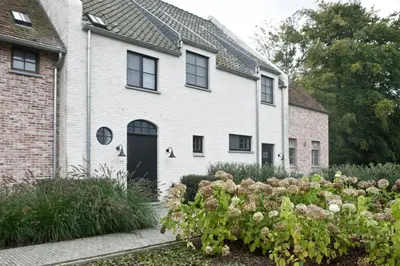 a white house with a black door and some flowers at B&B Interludium in Nijlen