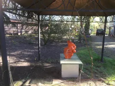 an orange statue sitting on a bench under a tent at Iosono by Moniek in Geel