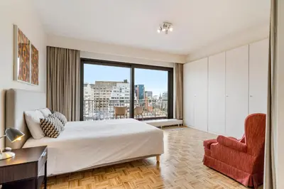 a bedroom with a bed and a chair and a large window at Fuths Loft Penthouse 85 in Antwerp