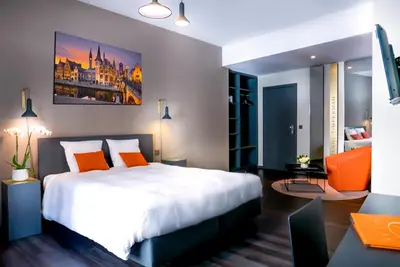 a bedroom with a large white bed and an orange chair at Atlas Hotel Brussels in Brussels