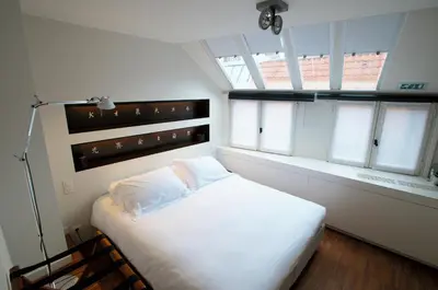 a bedroom with a large white bed with windows at Hotel Matelote in Antwerp