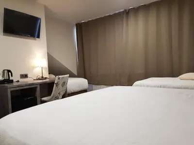 a hotel room with two beds and a desk at Hôtel Méribel in Brussels