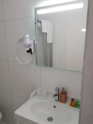 a white bathroom with a sink and a mirror at Hôtel Méribel in Brussels