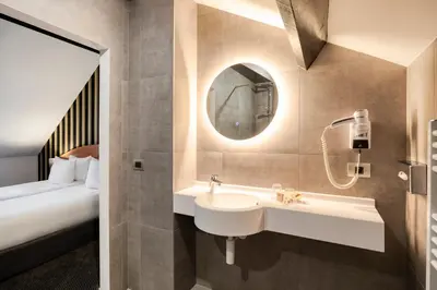 a bathroom with a sink and a mirror and a bed at Aris Grand Place Hotel in Brussels