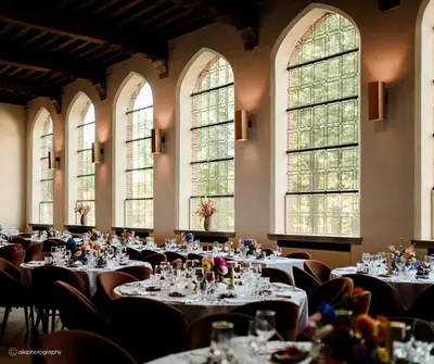 a large room with tables and chairs and windows at Priorij Corsendonk in Oud-Turnhout