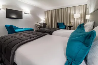 two beds in a hotel room with blue chairs at Martin's Château Du Lac in Genval