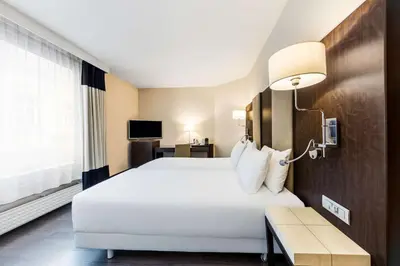 a hotel room with a large white bed and a table at NH Brussels Stéphanie in Brussels