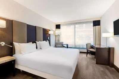 a hotel room with a large white bed and a desk at NH Brussels Stéphanie in Brussels