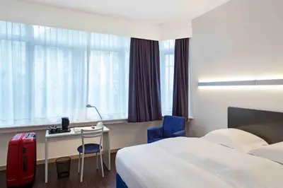 a hotel room with a bed and a desk with a red suitcase at Hôtel Argus by happyCulture in Brussels