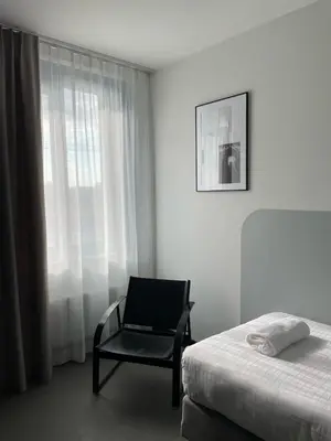 a bedroom with a bed and a chair next to a window at Hotel National Antwerp in Antwerp