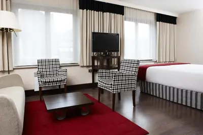 a hotel room with a bed and a tv and chairs at NH Brussels Grand Place Arenberg in Brussels