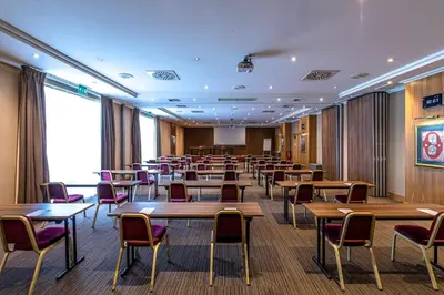 a conference room with tables and chairs and a screen at Holiday Inn Gent Expo by IHG in Ghent